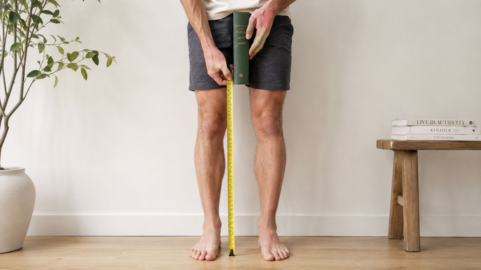 A person standing barefoot, using a yellow measuring tape to measure the inseam length.