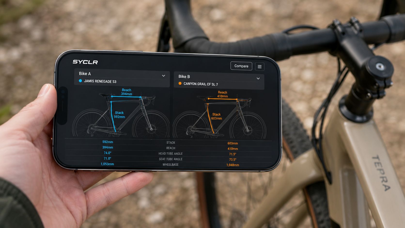 A hand holding a smartphone showing bike geometry comparison data between two gravel bikes on a display.