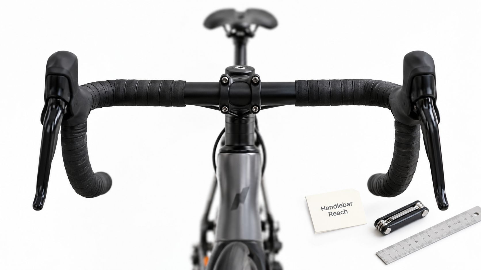 A top-down view of a road bike cockpit featuring handlebars, brake levers, a tool, and ruler.