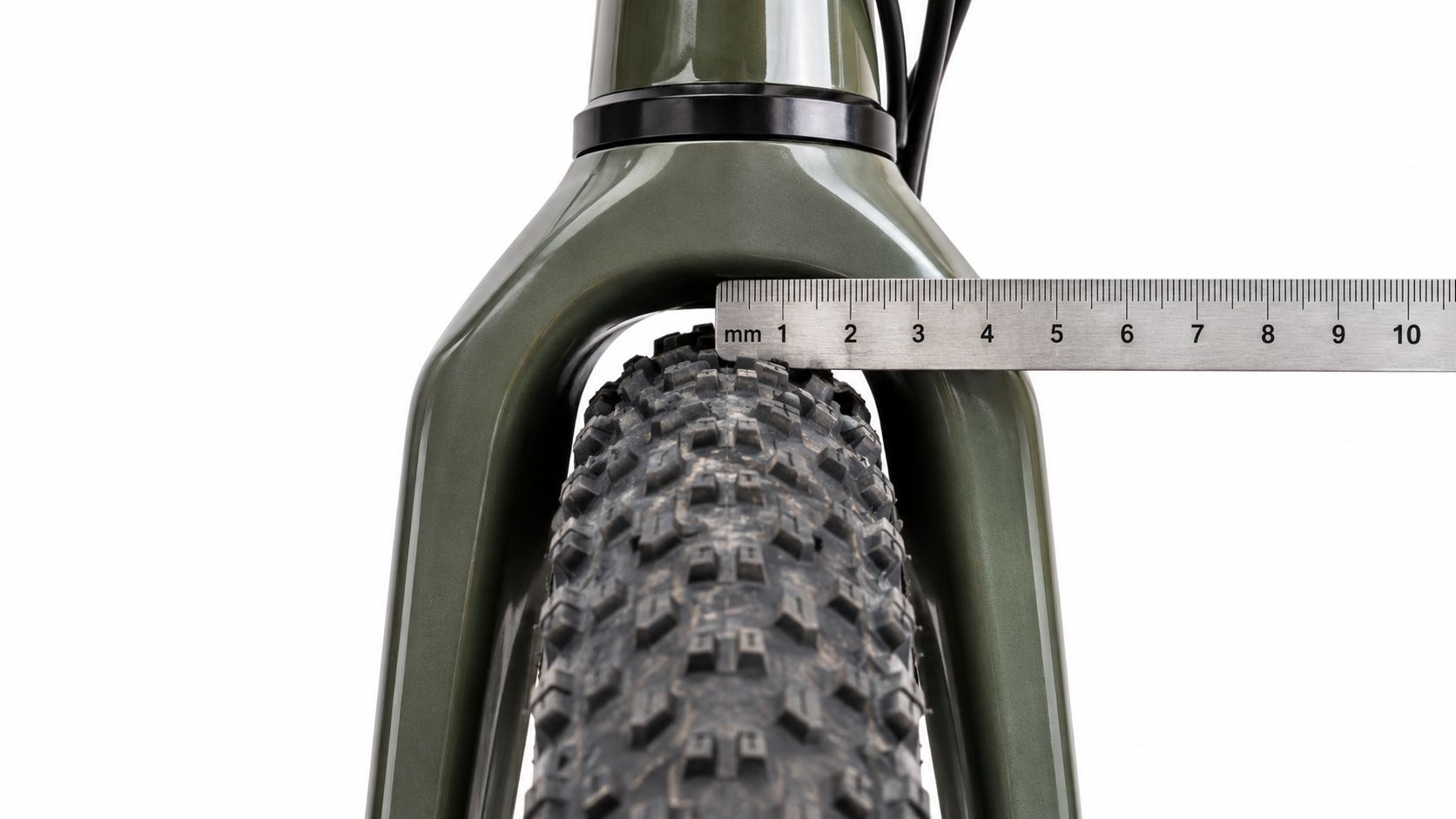 A close-up view of a bicycle tire clearance being measured with a metal ruler under the fork.